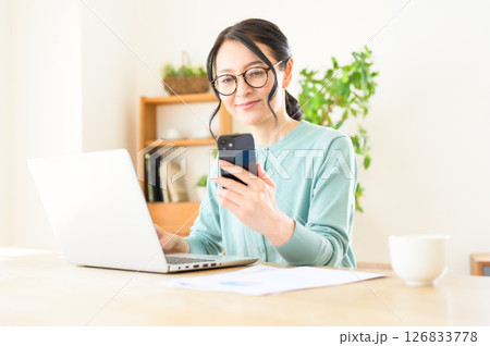 スマホを片手にパソコンで仕事中のミドル女性 126833778