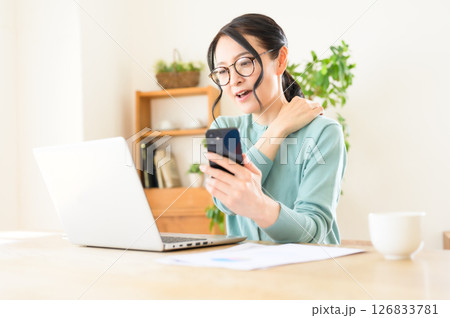 スマホを片手にパソコンで仕事中のミドル女性 スマホを片手にパソコンで仕事中のミドル女性 126833781