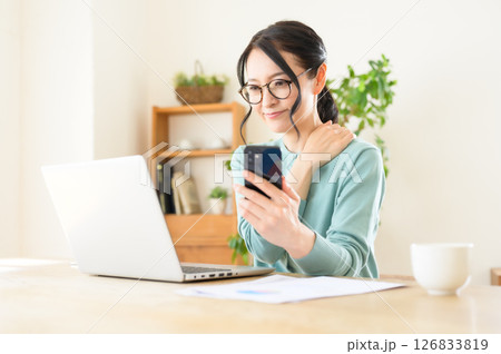スマホを片手にパソコンで仕事中のミドル女性 スマホを片手にパソコンで仕事中のミドル女性 126833819