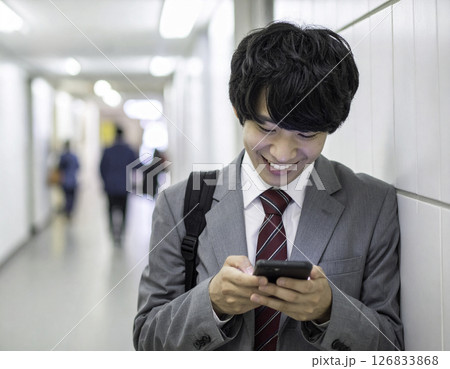 廊下でスマホを操作する男子高校生｜リラックスした笑顔の瞬間 126833868