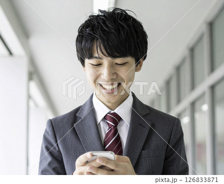 スマートフォンを操作しながら笑顔を見せる男子高校生｜爽やかで親しみやすい表情 126833871