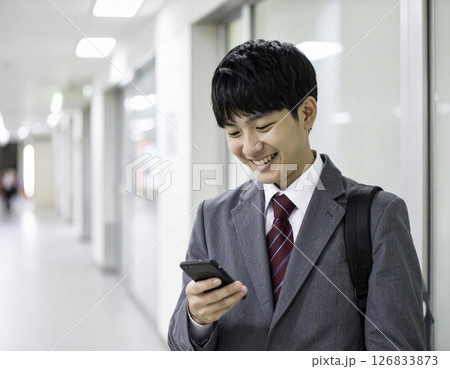 男子高校生がスマートフォンを見ながら笑顔を浮かべる廊下シーン 126833873