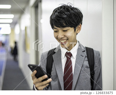 笑顔でスマホを見つめる男子高校生｜明るい廊下での一コマ 126833875
