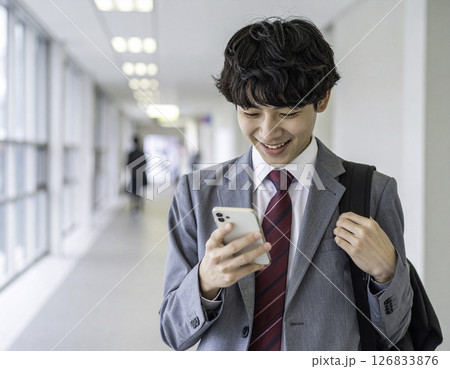 笑顔でスマホを見つめる男子高校生｜通路でのひととき 126833876