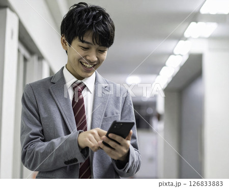 スマートフォンを操作しながら笑顔を見せる男子高校生 126833883