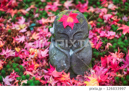 Jizo smiling Buddha with red fall maple leaf at enkoji temple, Kyoto Jizo smiling Buddha with red fall maple leaf at enkoji temple, Kyoto 126833997