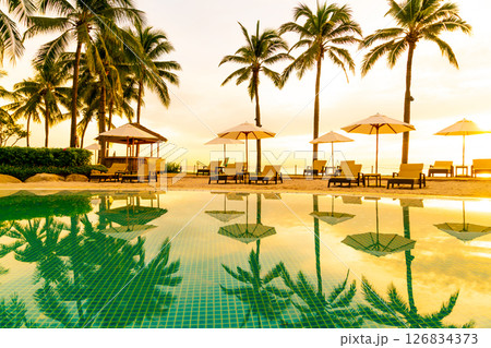 Umbrella and chair around swimming pool in hotel resort with sunrise in morning 126834373