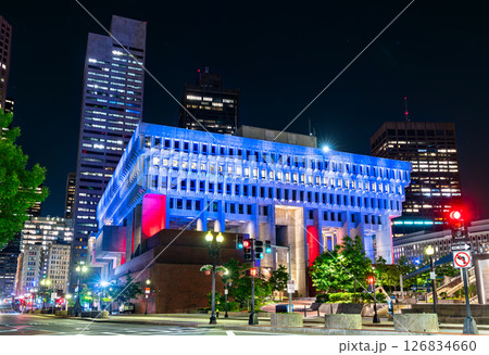 Nighttime view of Boston City Hall in Massachusetts, United States, illuminated in vivid red, white, and blue lighting. The brutalist concrete structure contrasts sharply with the surrounding 126834660