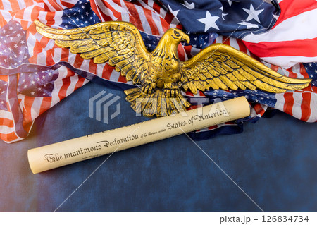 Rolled Declaration of Independence lies beside an eagle emblem on patriotic fabric, symbolizing American history. 126834734