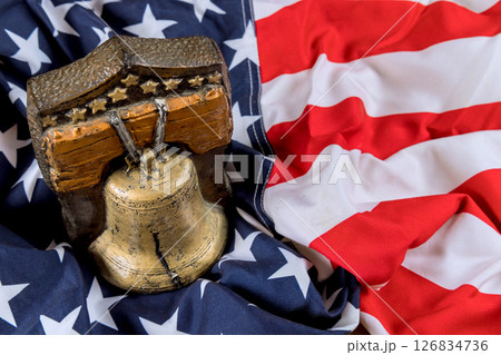 Ornate bell remembrance symbol is placed on folded American flag, highlighting themes of freedom national identity. 126834736