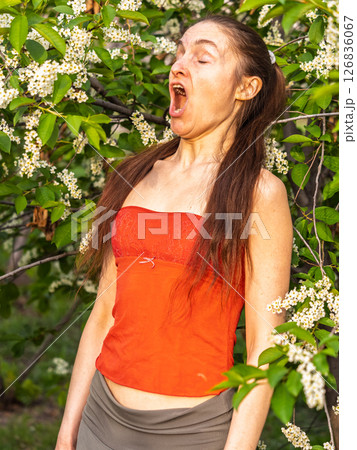 Young woman sneezes in the park against the background of a flowering tree. Allergy to pollen concept. Young woman sneezes in the park against the background of a flowering tree. Allergy to pollen concept. 126836067