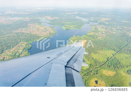 View of airplane wing, blue skies and green land during landing. Airplane window view. 126836885