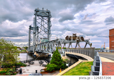 View of Memorial Bridge spanning the Piscataqua River between Portsmouth, New Hampshire and Kittery, Maine, featuring steel trusses, a lift section, and a small riverside plaza under cloudy skies View of Memorial Bridge spanning the Piscataqua River between Portsmouth, New Hampshire and Kittery, Maine, featuring steel trusses, a lift section, and a small riverside plaza under cloudy skies 126837206
