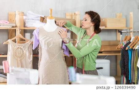 Woman tailor connects parts of dress on mannequin Woman tailor connects parts of dress on mannequin 126839490