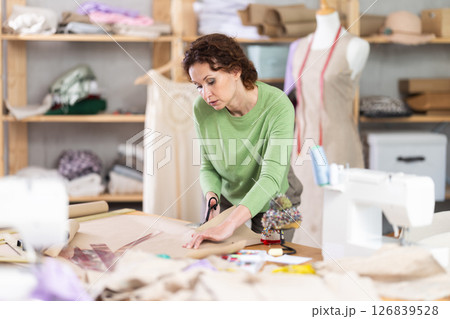 Female tailor cutting paper with scissors, cutting out the outline of pattern for a dress 126839528