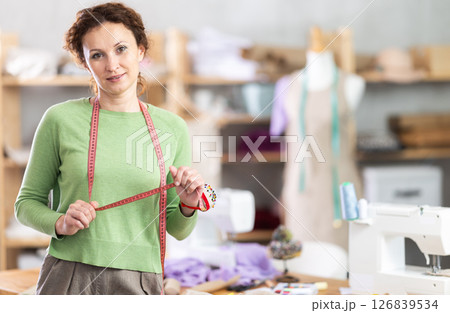 Female tailor with measuring tape posing in sewing studio 126839534