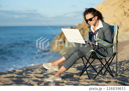 Businesswoman in office clothes working on laptop on seashore 126839651