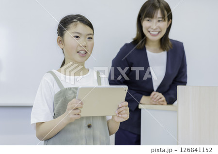 タブレットを持って発表する小学生の女の子と先生 撮影協力:学校法人電波学園 東京電子専門学校 タブレットを持って発表する小学生の女の子と先生 撮影協力:学校法人電波学園 東京電子専門学校 126841152