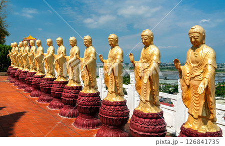 Striking row of golden Buddha statues aligned in front of a traditional red-tiled corridor at Fo Guang Shan Monastery in Kaohsiung, Taiwan. The figures stand in peaceful poses beneath an ornately 126841735
