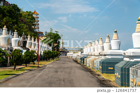 Symmetrical rows of white stupas line a quiet pathway at Fo Guang Shan Monastery in Kaohsiung, Taiwan, with a traditional Chinese pagoda visible through the trees under a clear blue sky Symmetrical rows of white stupas line a quiet pathway at Fo Guang Shan Monastery in Kaohsiung, Taiwan, with a traditional Chinese pagoda visible through the trees under a clear blue sky 126841737