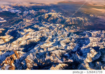Aerial view of the snow-covered Sierra Nevada mountains in California during sunset, revealing dramatic peaks and rugged terrain with golden light highlighting the landscape 126841739