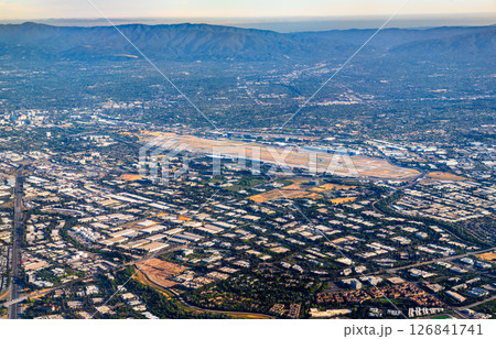 Aerial panorama of San Jose Mineta International Airport in California, showing its runways surrounded by a grid of industrial buildings, residential areas, and the Santa Clara Valley foothills in the Aerial panorama of San Jose Mineta International Airport in California, showing its runways surrounded by a grid of industrial buildings, residential areas, and the Santa Clara Valley foothills in the 126841741