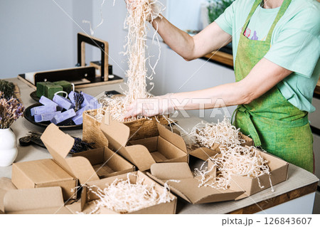 Person fills kraft boxes with shredded paper as part of eco-conscious soap packaging. Intentional packaging, unboxing ritual, sensory filler, slow commerce Person fills kraft boxes with shredded paper as part of eco-conscious soap packaging. Intentional packaging, unboxing ritual, sensory filler, slow commerce 126843607