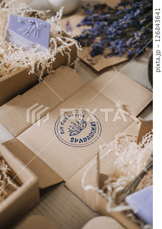 Open kraft box with stamped spa branding surrounded by handmade lavender soaps and shredded filler. Artisanal branding, handmade soap, craft identity, eco packaging 126843641