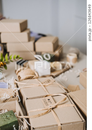 Table filled with kraft spa gift boxes containing handmade soaps and natural fillers. Spa gift box, handmade wellness products, calming rituals, stress relief gifts Table filled with kraft spa gift boxes containing handmade soaps and natural fillers. Spa gift box, handmade wellness products, calming rituals, stress relief gifts 126843649