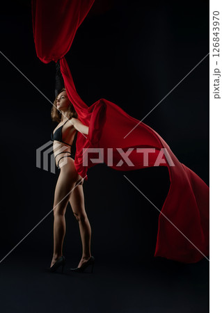 Model posing confidently with red fabric in a dramatic casting shoot 126843970