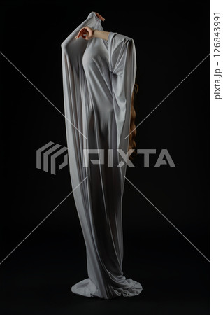 Model poses dramatically in flowing garment against black backdrop 126843991