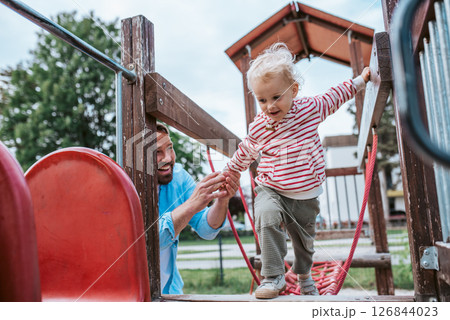 Toddler crossing playground obstacle with dad's support Toddler crossing playground obstacle with dad's support 126844023