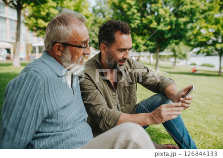 Son showing older father something in smartphone, sharing a joyful moment . 126844133