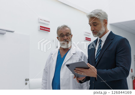 Doctor talking with hospital manager, showing him document in tablet. Doctor talking with hospital manager, showing him document in tablet. 126844169