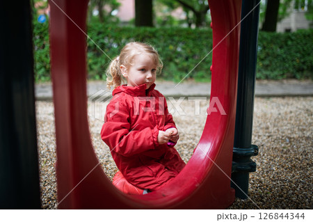 Child in red coat resting at play area. Child in red coat resting at play area. 126844344