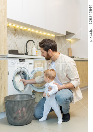 Young caucasian guy and his little son sorting clothes before putting into washing machine 126845644