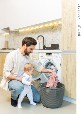 Young caucasian guy and his little son sorting clothes before putting into washing machine Young caucasian guy and his little son sorting clothes before putting into washing machine 126845647
