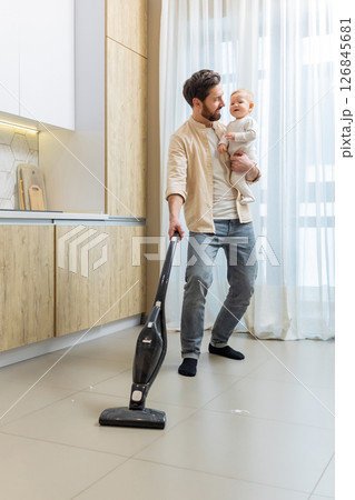 Young single dad cleaning the house while holding his son in his hands 126845681