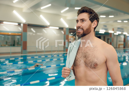 Bearded caucasian young man standing in the pool with a towel on his shoulder Bearded caucasian young man standing in the pool with a towel on his shoulder 126845868