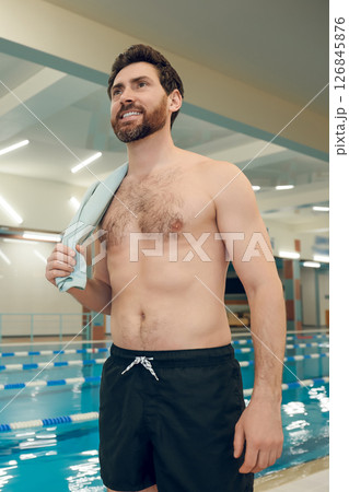 Bearded caucasian young man standing in the pool with a towel on his shoulder Bearded caucasian young man standing in the pool with a towel on his shoulder 126845876