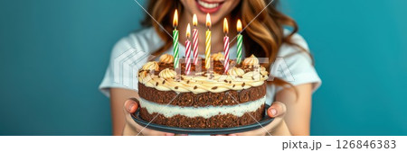 Celebrating with a beautifully decorated birthday cake and colorful candles held by a joyful young woman indoors 126846383