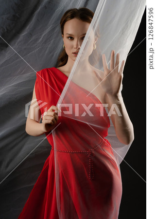 Woman poses in a studio wearing a striking red dress while expressing deep emotion through her gesture and gaze 126847596
