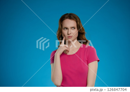 Woman posing thoughtfully in a studio setting with an emotional expression against a bright blue background Woman posing thoughtfully in a studio setting with an emotional expression against a bright blue background 126847704