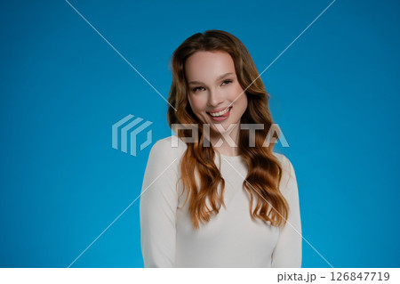Woman posing with a joyful expression in a studio setting against a vibrant blue backdrop 126847719
