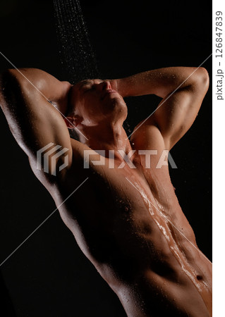 Man enjoying a shower under a stream of water in a dark setting 126847839