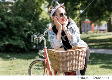 Portrait young adult pretty woman with red vintage retro bike and pin-up casual outfit green city park bright sunny summer day. Happy beautiful female person cycling outdoors. Healthy lifestyle 126848823