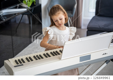 Little girl playing piano at home in the living room. Childhood creativity and musical development in cozy family environment Little girl playing piano at home in the living room. Childhood creativity and musical development in cozy family environment 126849961