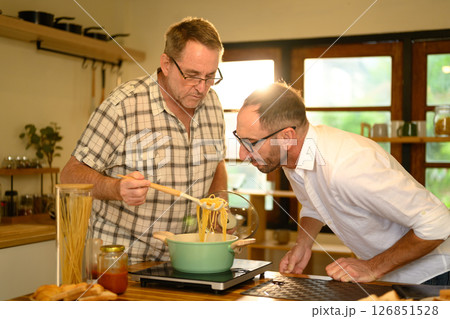 Happy senior man and grown son preparing pasta dish in a bright kitchen. Father day concept 126851528