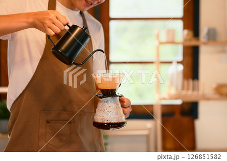 Man wearing an apron preparing fresh pour over coffee in a cozy kitchen 126851582