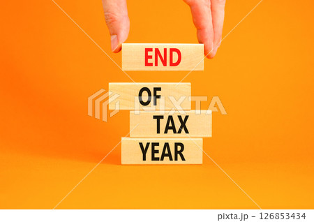 End of tax year symbol. Concept words phrase End of tax year on beautiful wooden blocks. Beautiful orange paper background. Businessman's hand. Business End of tax year concept. Copy space. End of tax year symbol. Concept words phrase End of tax year on beautiful wooden blocks. Beautiful orange paper background. Businessman's hand. Business End of tax year concept. Copy space. 126853434